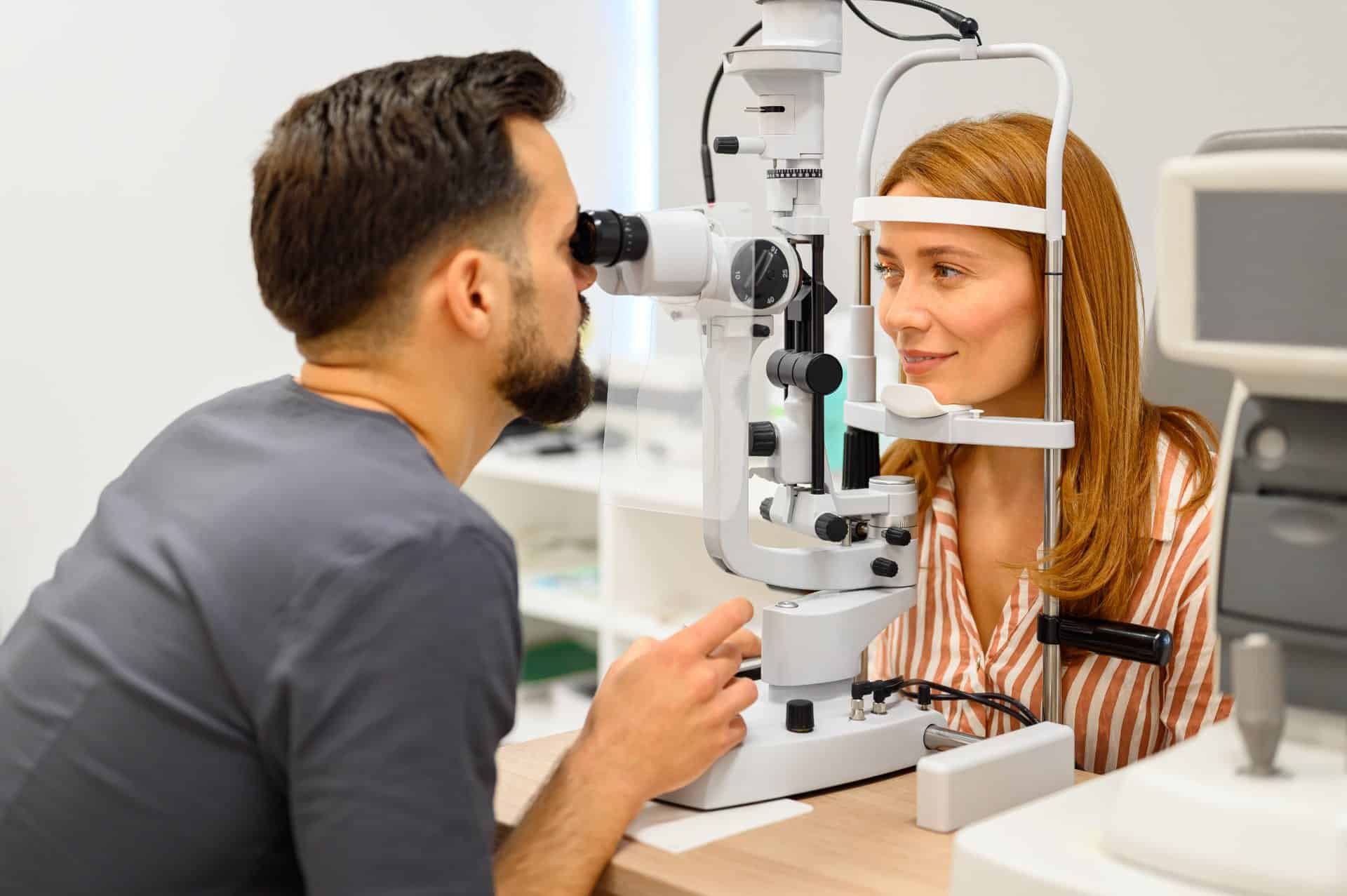 Male ophthalmologist conducting slit lamp eye exam on female patient during checkup at modern vision care clinic
